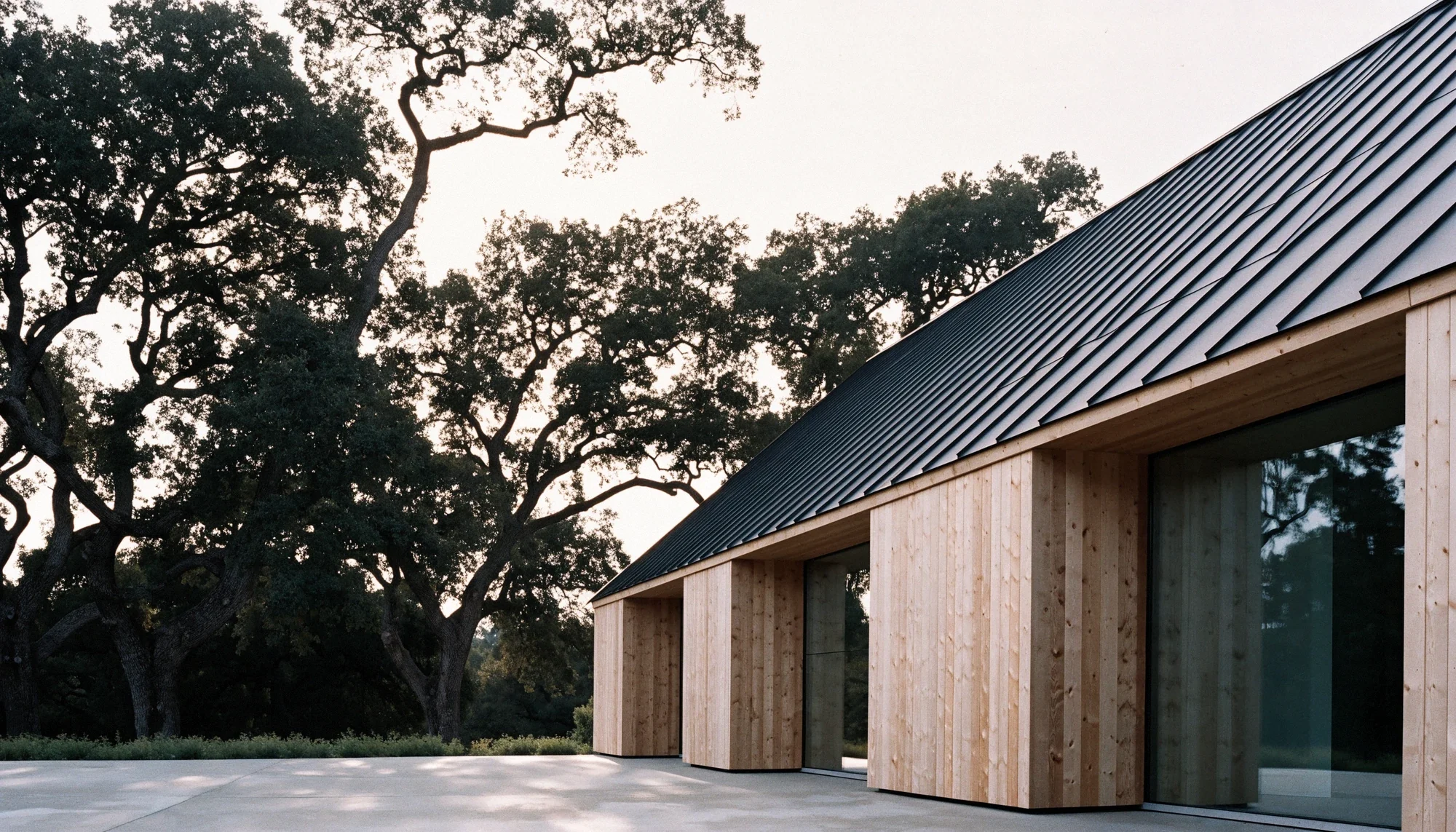 Timber-clad home with a dark metal roof beneath mature oak trees